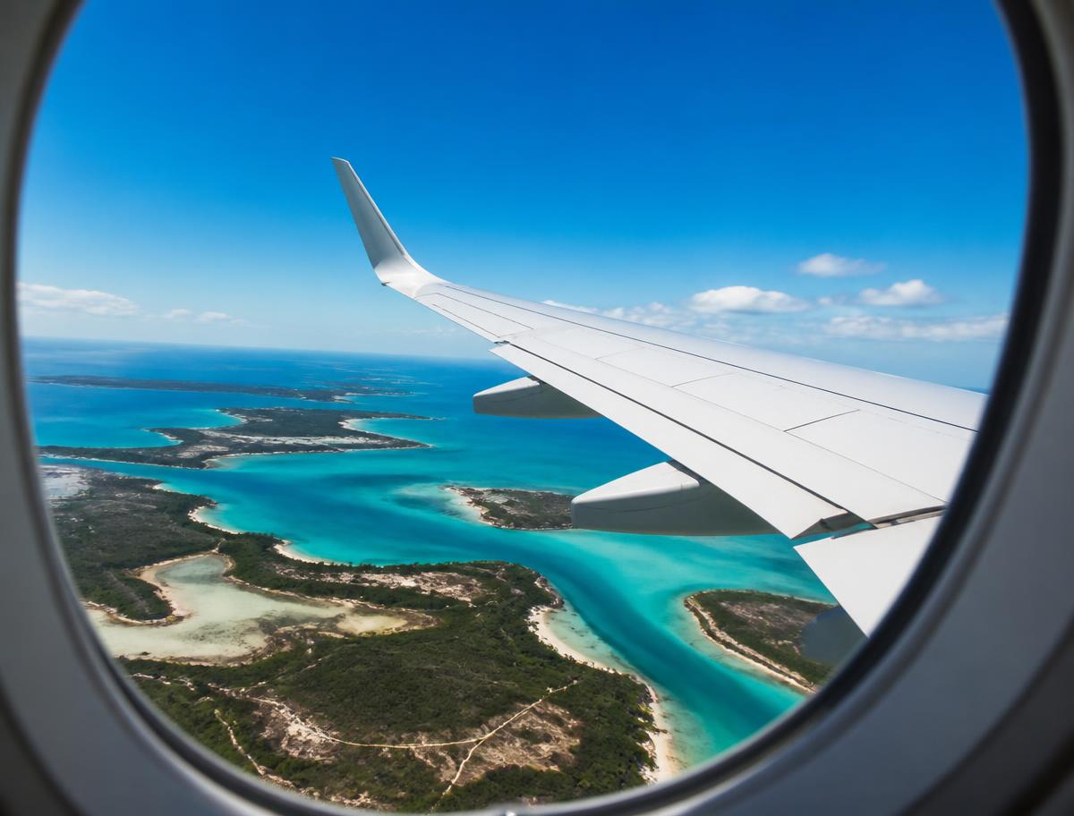 View of an unbranded aircraft wing over turquoise Caribbean islands from a cabin window