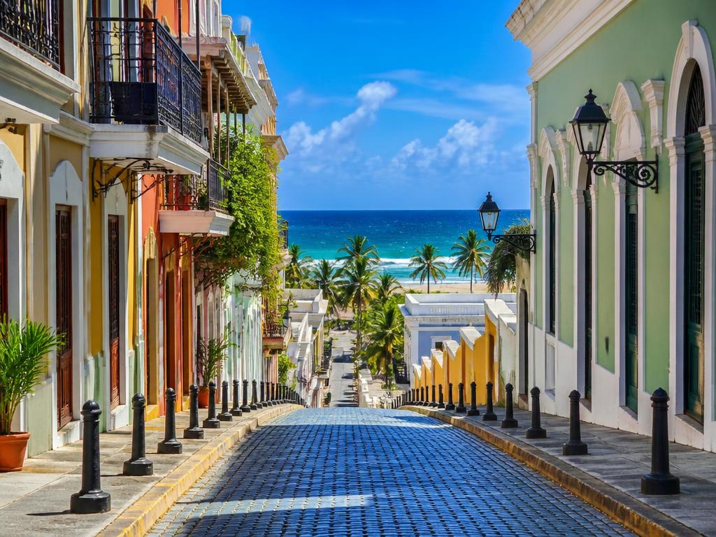 Blue cobblestone street in Old San Juan leading down to palm trees and the ocean